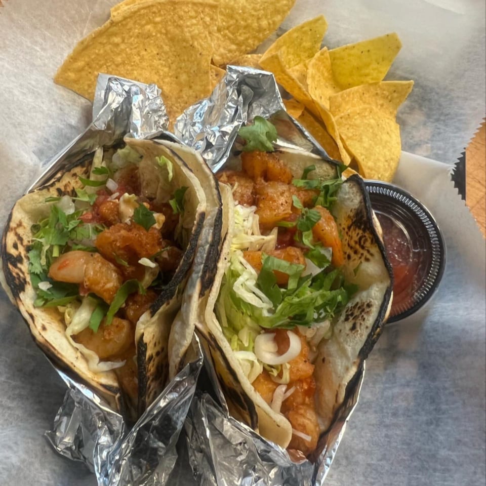 Two shrimp tacos with cilantro, lettuce, and sauce, alongside tortilla chips and salsa.