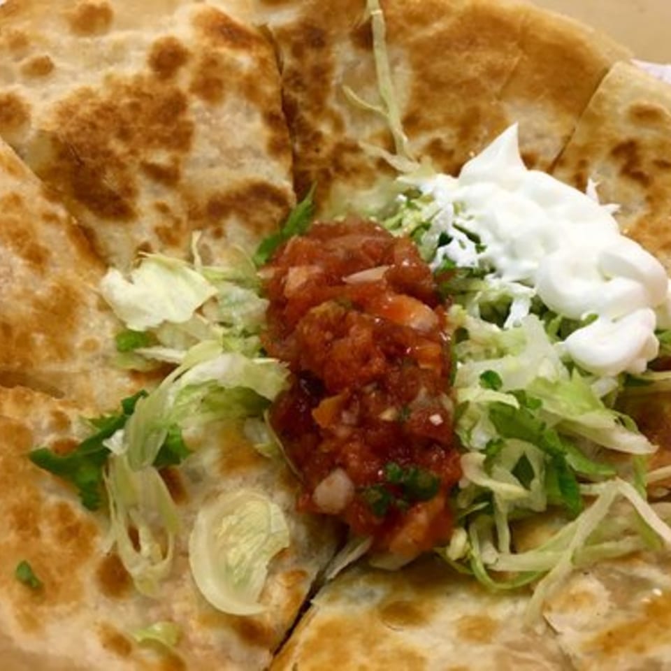 A Badlands Tacos quesadilla, cut into wedges, topped with salsa, shredded lettuce, and sour cream.