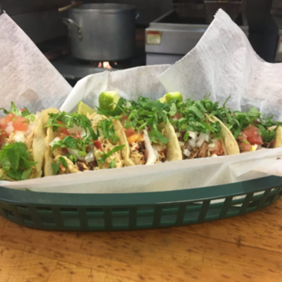 A basket of Badlands Tacos, filled with meat, cilantro, onions, and lime wedges.
