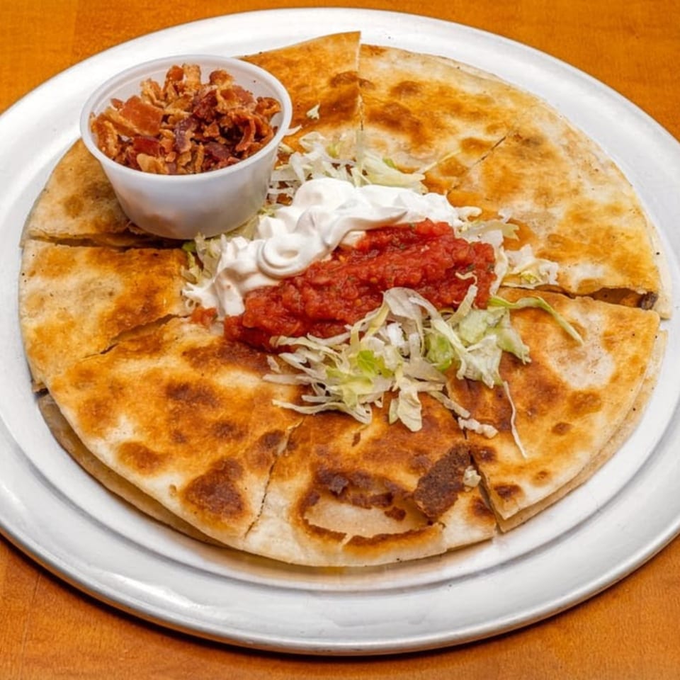 Badlands Tacos quesadilla with salsa, sour cream, shredded lettuce, and a side of bacon bits.