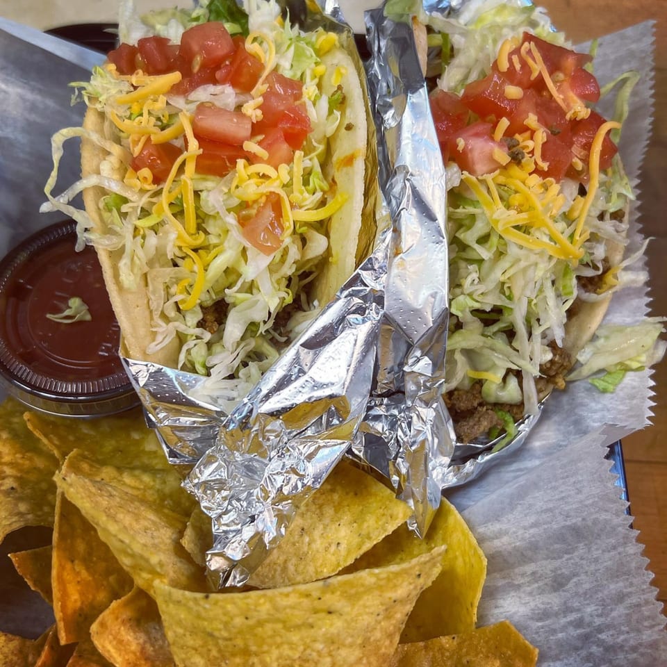 Two Badlands Tacos with shredded lettuce, cheese, and diced tomatoes, served with tortilla chips and salsa.